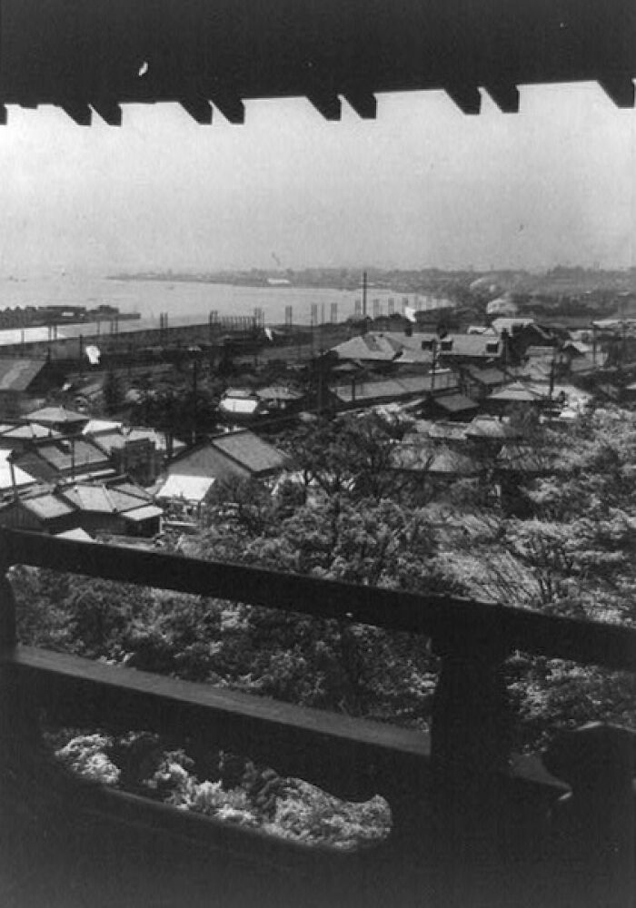 View of a historic Japanese townscape and coastline in the 1800s, showing traditional buildings and natural surroundings.