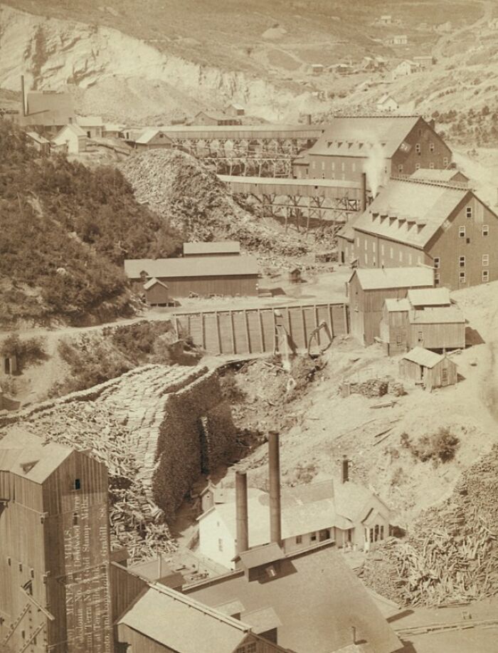 Vintage 1800s industrial site with large wood piles and buildings, reflecting the era of cowboys and Native Americans.