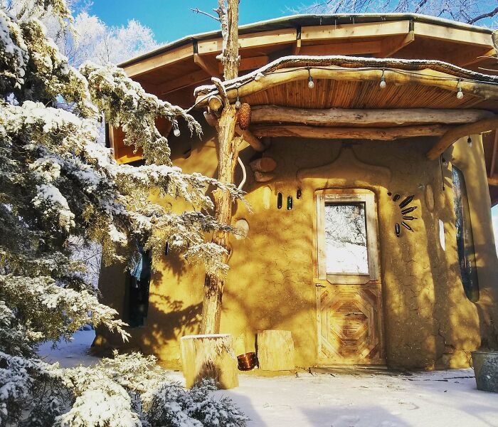 Rustic tiny home with natural wood and mud walls surrounded by snowy trees, showcasing unique tiny homes off the grid living.