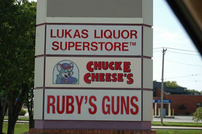 Sign showing businesses including a liquor store, Chuck E Cheese’s, and a gun shop, reflecting current life in the US.