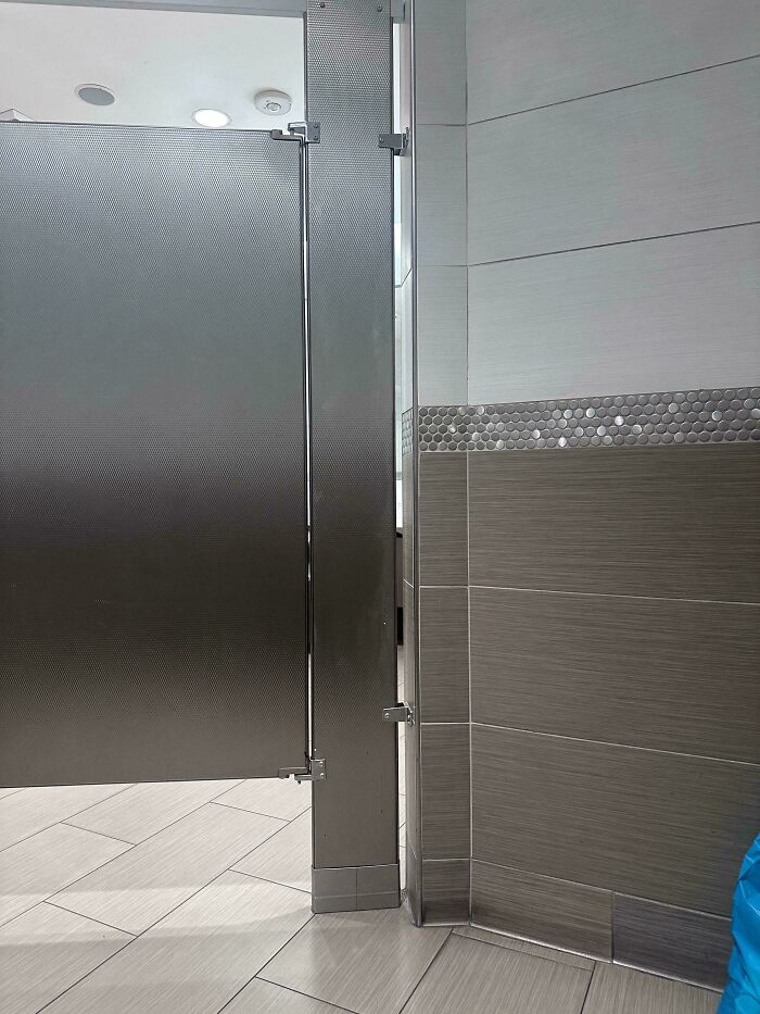 Partial view of a public restroom stall door and tiled floor capturing everyday life in the US through American eyes.