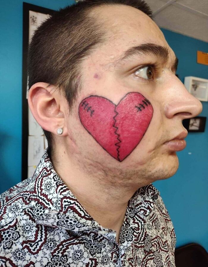 Man with a large red broken heart tattoo on his cheek, showcasing one of many wild tattoo fails.