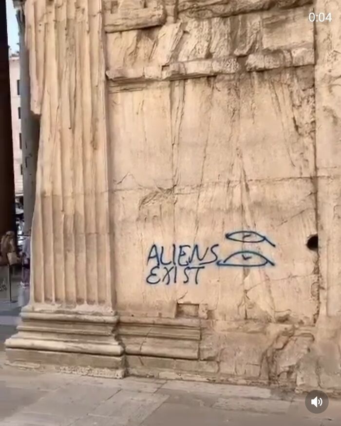 Graffiti saying aliens exist on an ancient stone wall, showing rude behavior of entitled tourists at historical sites.