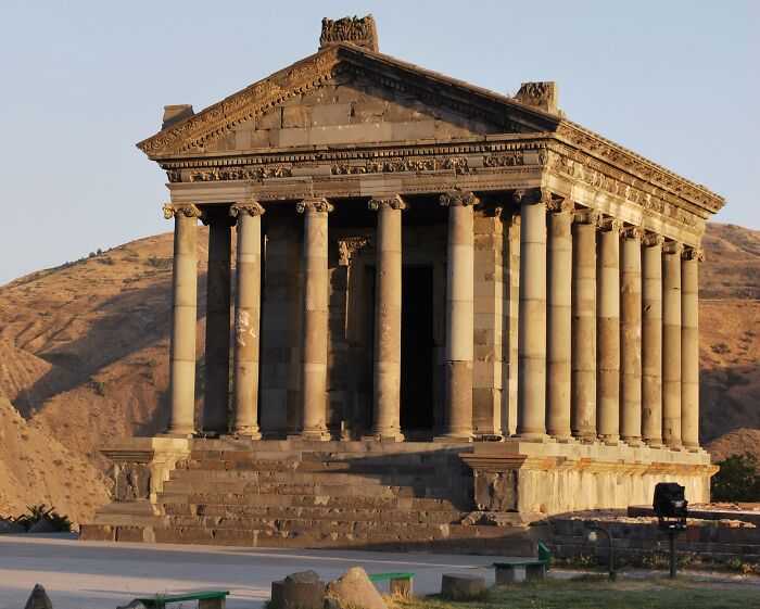 Ancient man-made structure with tall columns and triangular pediment set against a mountainous background at sunset.