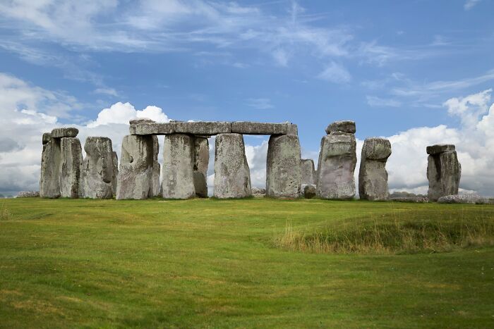 Stonehenge ancient man-made structure on a grassy field under a partly cloudy blue sky in England.