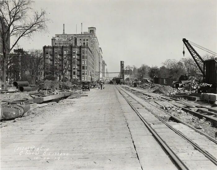Black and white photo showing life in America 100 years ago with old buildings, construction site, and railroad tracks.