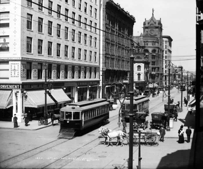 Historic streetcar and horse-drawn carriage on busy city street showing life in America 100 years ago.