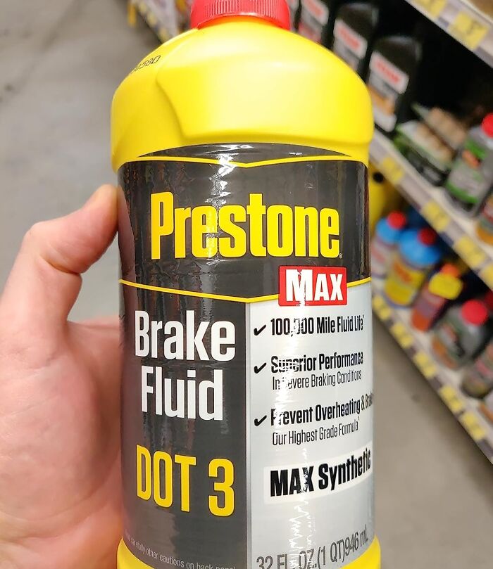 Hand holding a bottle of Prestone DOT 3 brake fluid on a store aisle with practical car advice for maintenance.