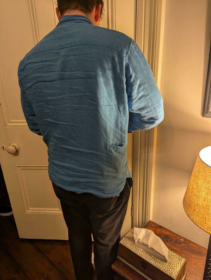 Person in a blue shirt standing near a door in a dimly lit room with a lamp and wooden table nearby mystery objects.