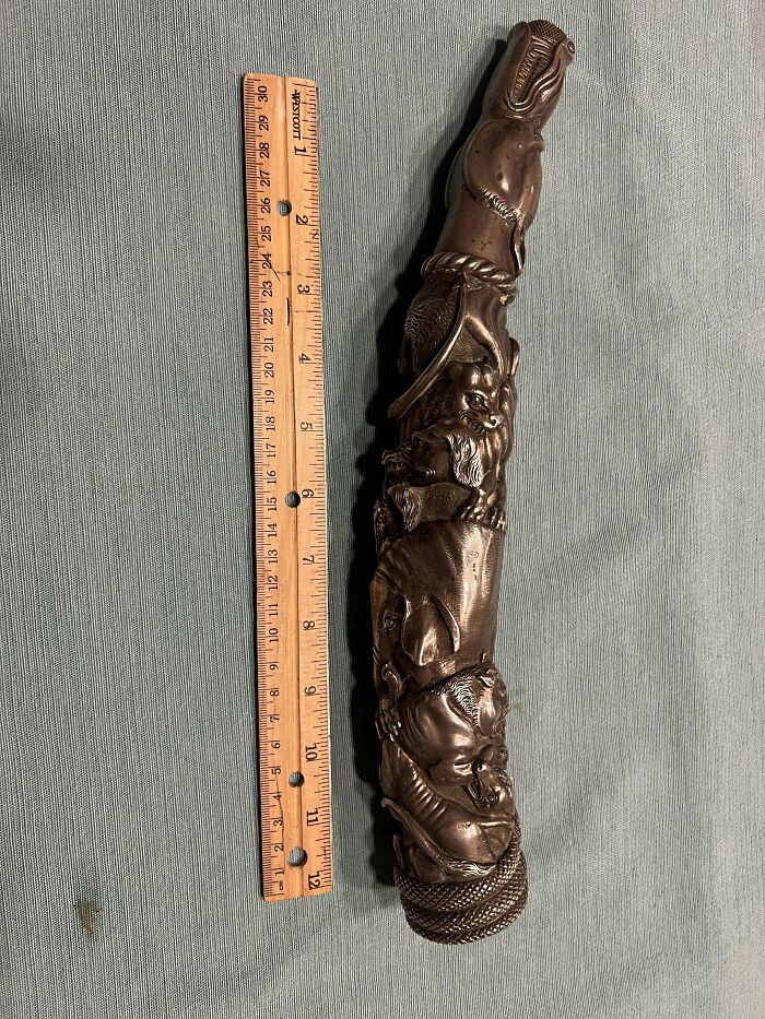 Carved mystery object with animal figures next to a wooden ruler for size, from an online group recognizing mystery objects.