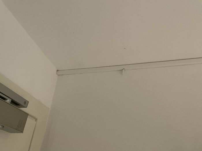 Corner of a white room showing a white plastic strip with a hook, an example of a mystery object to recognize.