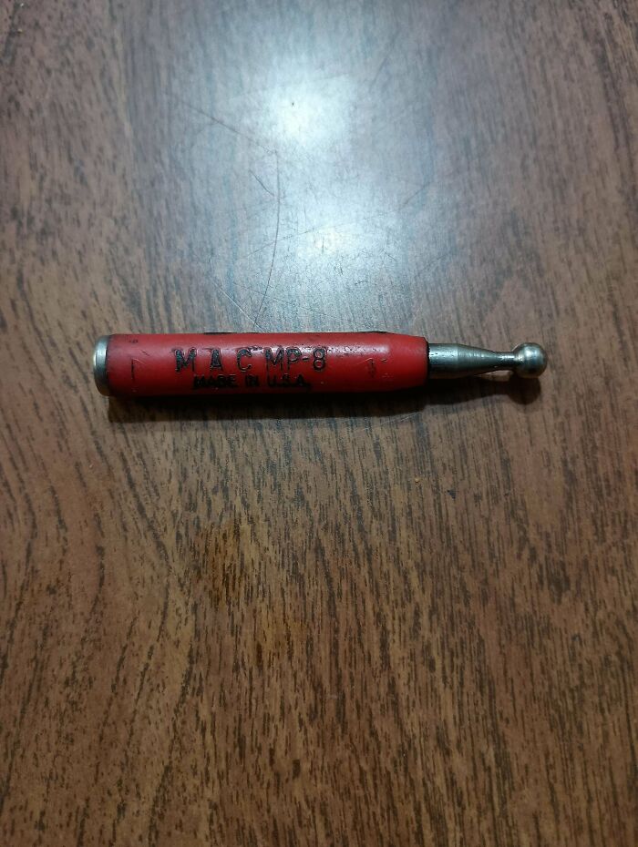 Small red mystery object with a metal ball tip labeled MAC MP-8 on a wooden surface, from a group recognizing mystery objects