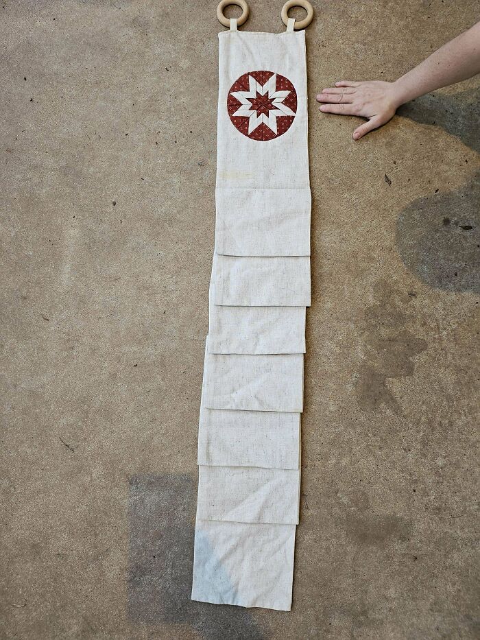 Long beige fabric organizer with red star pattern and wooden rings laid flat on concrete floor mystery objects