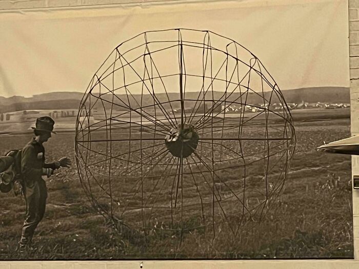 Man in vintage clothing examines large wireframe spherical object in field, a mystery object recognized by online group.