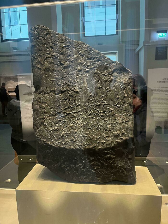 Ancient stone artifact displayed in a museum with visitors in the background, showcasing alternate angles of historic places.