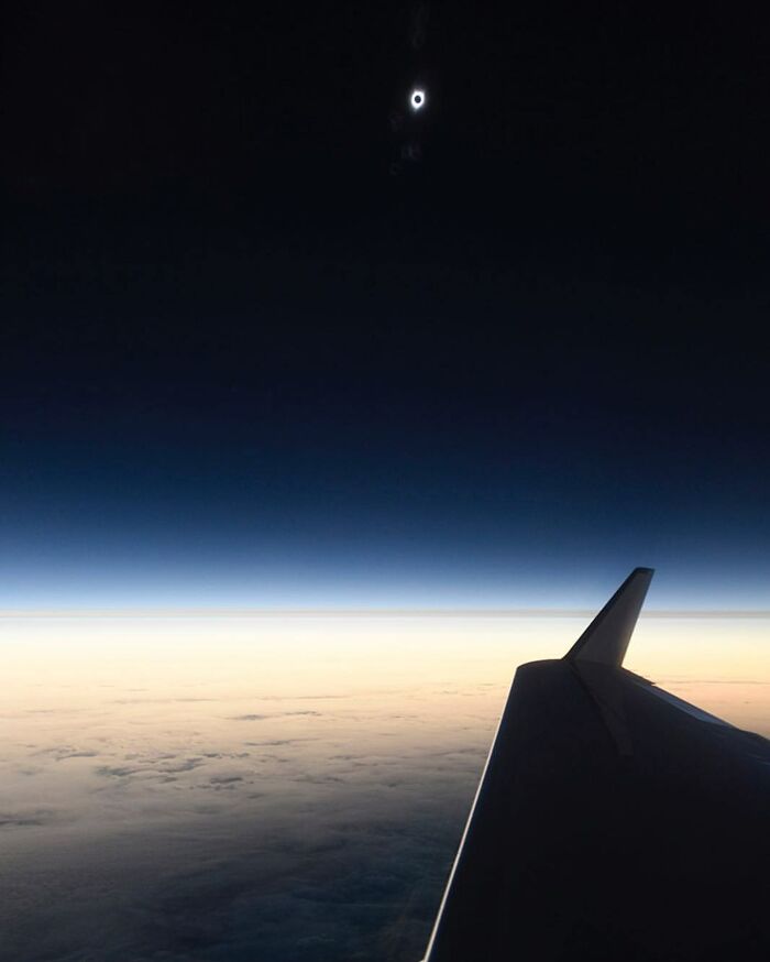 View from airplane wing showing a solar eclipse above the Earth's horizon in a unique alternate angle of an iconic event.