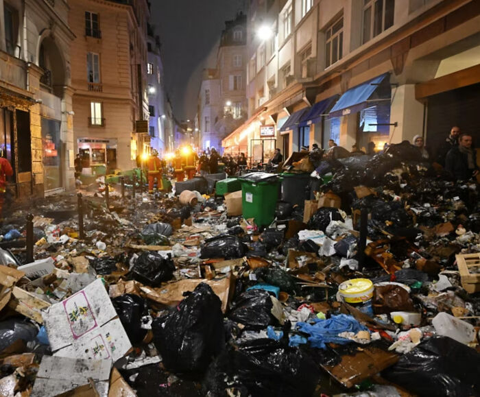 Street filled with piles of garbage and trash bags at night showing alternate angles of iconic events and places in history.