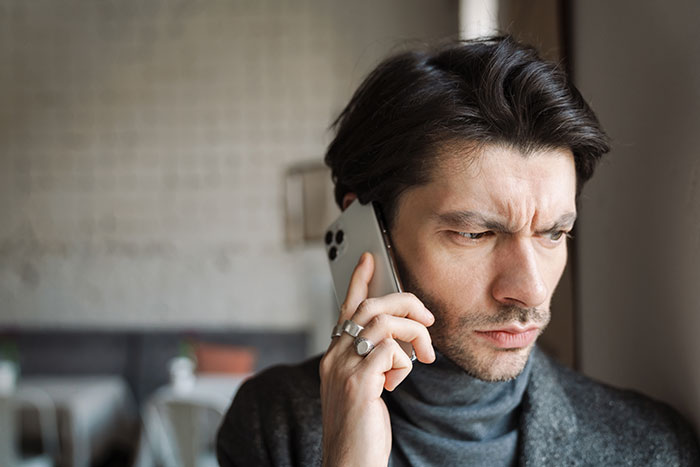 Man on phone looking concerned, wearing a dark sweater, related to woman dumping boyfriend over heiress dispute.