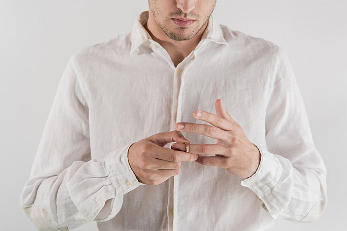 Man in a white shirt removes a wedding ring, reflecting tension in marriage.