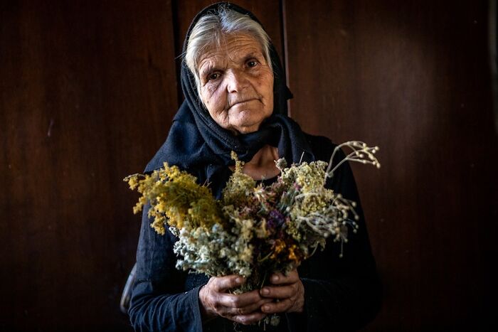 Elderly woman in a headscarf holding dried flowers, expressing vulnerability of aging, photographed by Michele Zousmer.