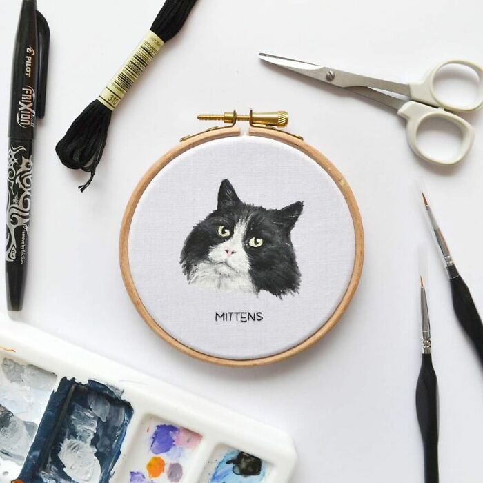 Embroidery of a black and white cat named Mittens, with thread, scissors, and art tools nearby.