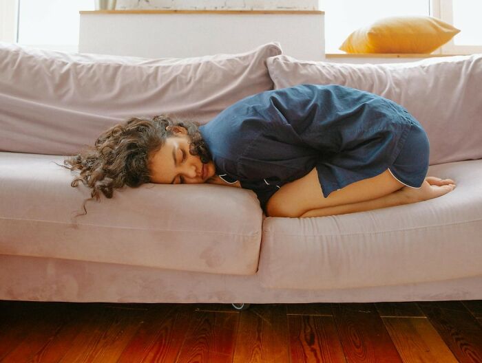 Woman in discomfort on sofa; highlights gender disparity in pain medication prescriptions.