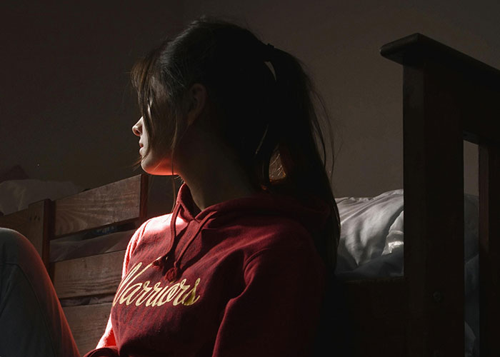 Young woman in a dimly lit room sitting on a bed, reflecting heartbroken feelings about cheating in a relationship.