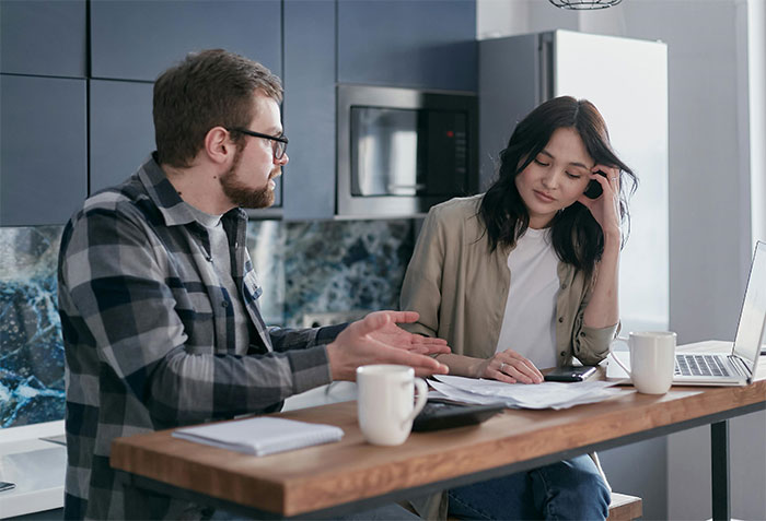 Couple discussing lottery winnings at kitchen table, appearing thoughtful and serious.