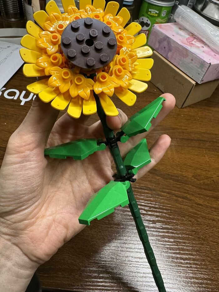 A hand holds a sunflower made of toy bricks, showcasing Easter treasures creativity.