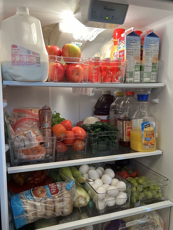 Clear plastic bins neatly organizing fruits, vegetables, and beverages inside a well-arranged refrigerator.