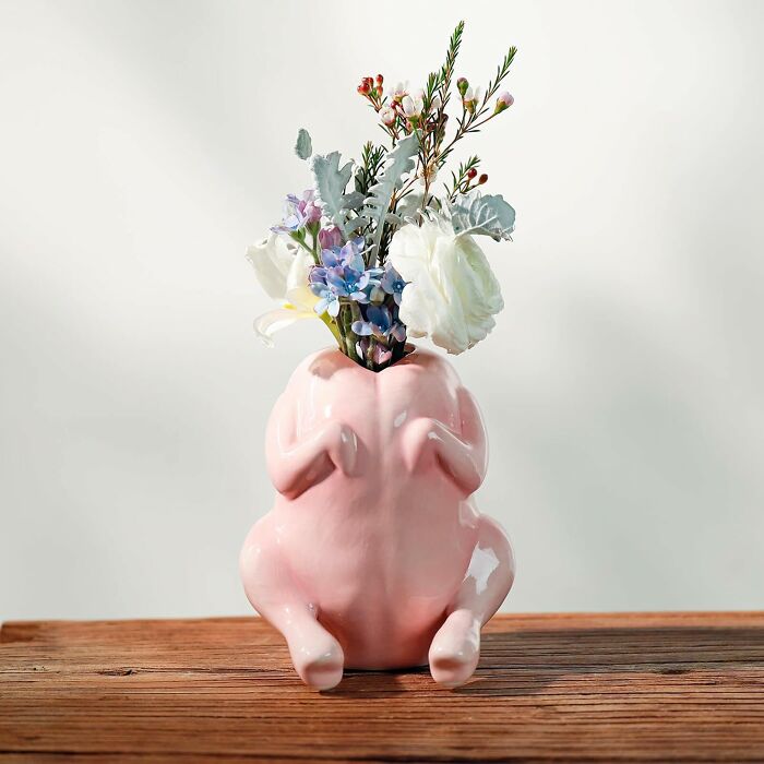 Pink ceramic turkey-shaped vase holding assorted flowers on a wooden surface, a funny Mother's Day gift idea.