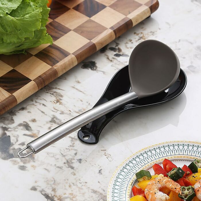 Silicone ladle with stainless steel handle resting on a black spoon rest near a cutting board, perfect for kitchen deals haul.