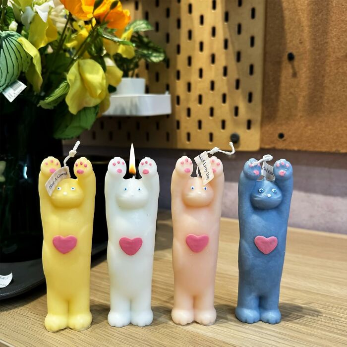 Cute cat-shaped candles with pink hearts, showcasing unique wax art on a wooden surface with flowers in the background.