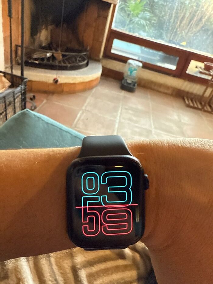 A smartwatch displaying the time 03:59, with a modern design and colorful numbers in a cozy living room setting.