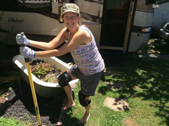 A woman smiles while gardening next to an RV, demonstrating a relaxed gardening style.