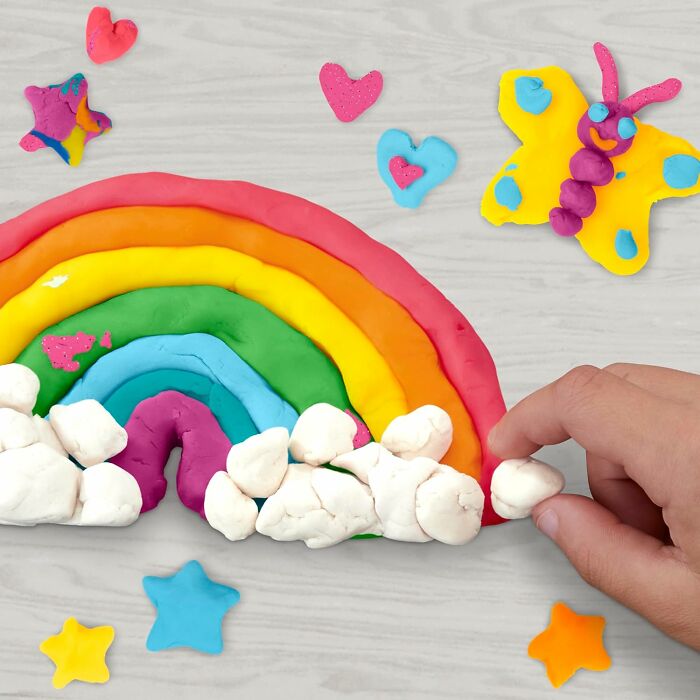 Colorful modeling clay shaped into a rainbow, butterfly, stars, and hearts with a child's hand playing, showcasing popular kids toys.