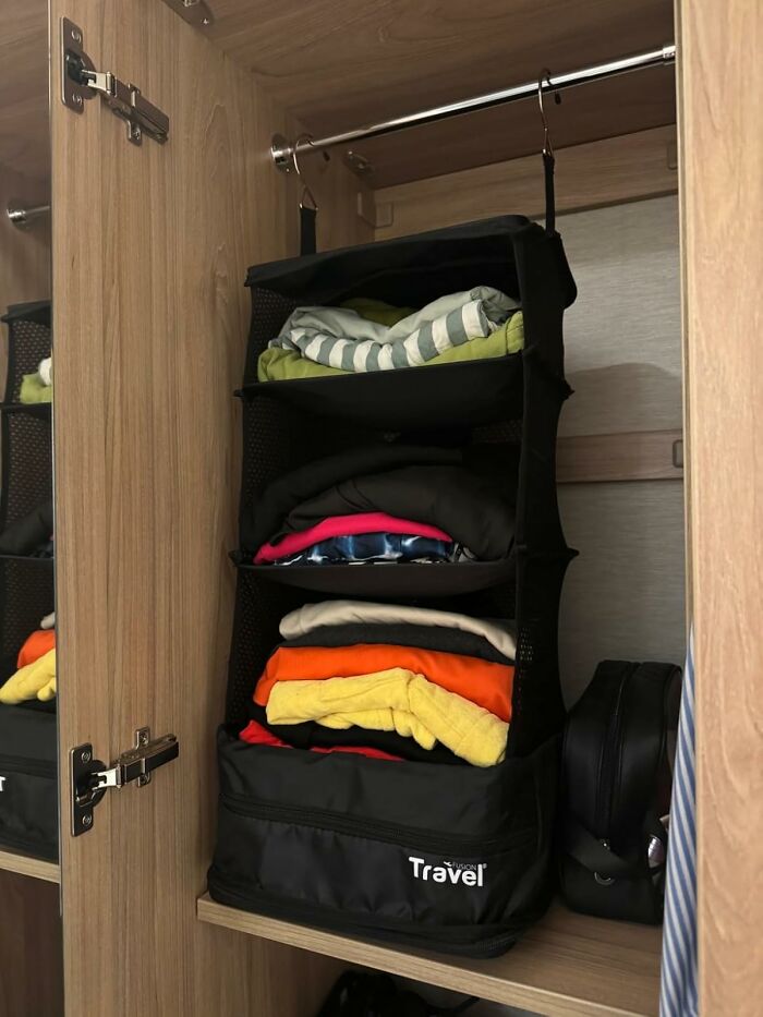 Hanging travel organizer with clothes in a wooden wardrobe, showcasing useful travel picks for budget-friendly vacations.