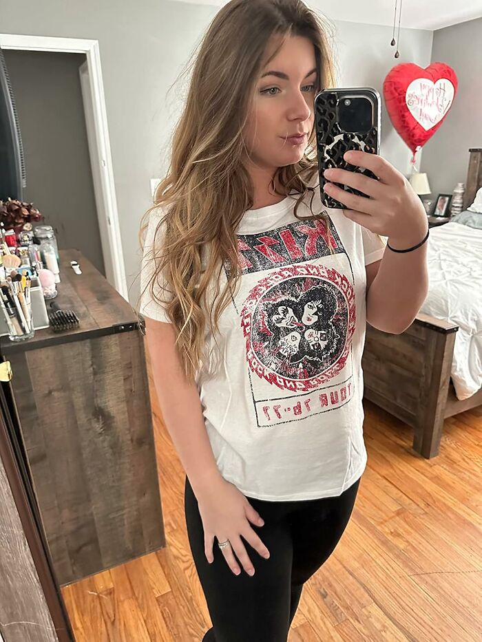 Millennial fashion urge: woman in graphic tee taking a selfie in her room.
