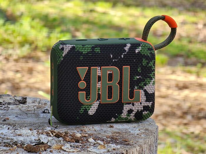Camouflage JBL speaker on a tree stump, perfect for your festival survival kit.
