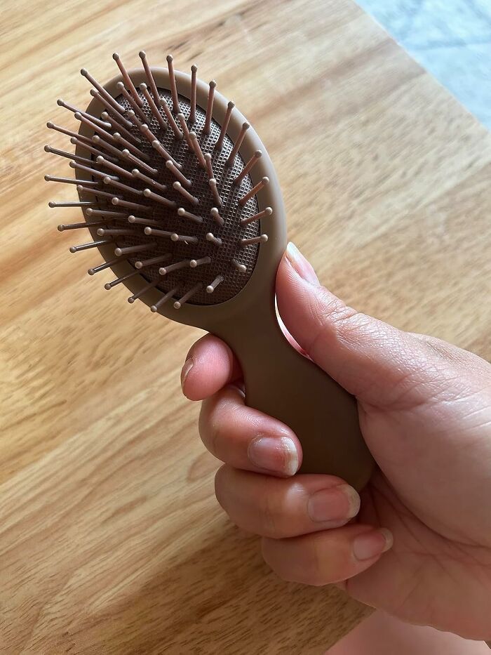 Compact travel-friendly hairbrush held in hand, ideal for budget-conscious vacationers.
