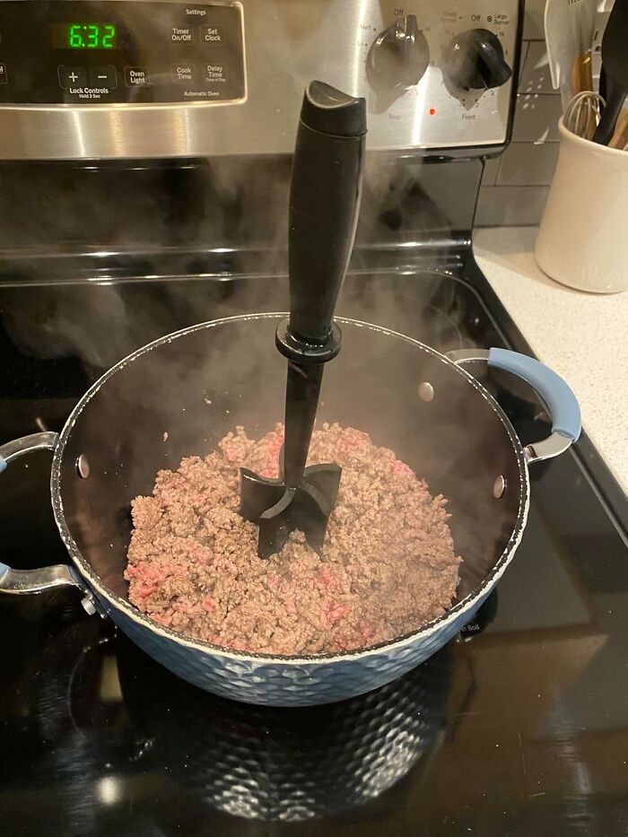 Pot of steaming ground beef on stovetop with a meat chopper, simplifying meal prep.