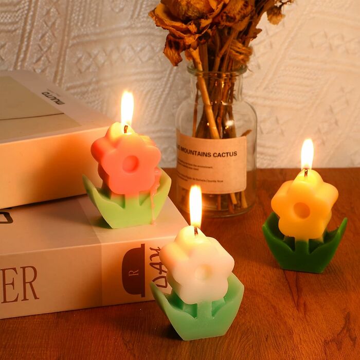 Colorful flower-shaped wax candles lit on a table, showcasing unique designs.
