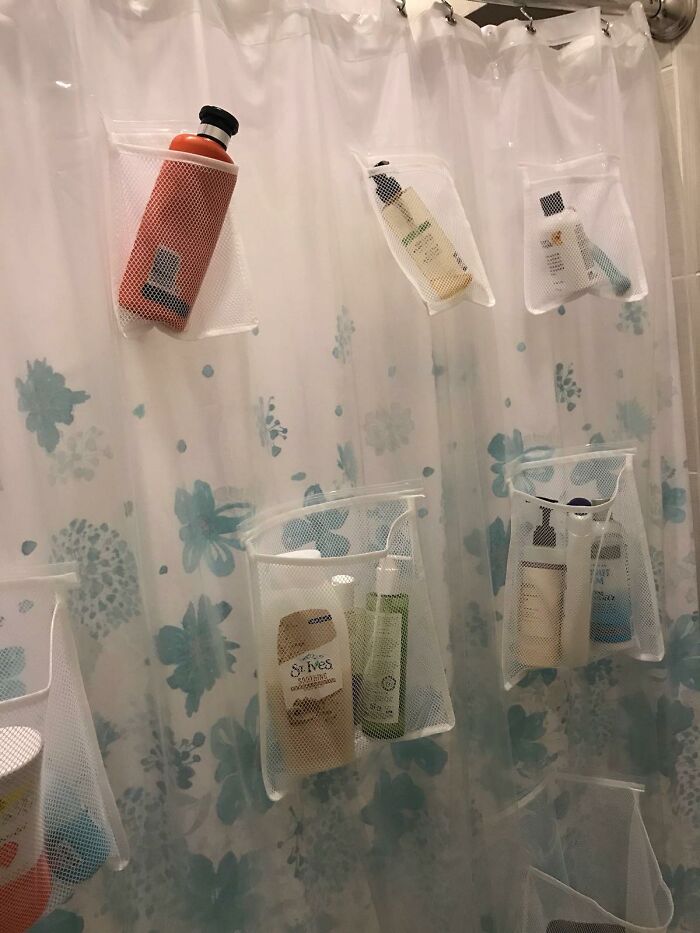 Mesh shower caddies hanging on a floral shower curtain, organizing various bathroom must-haves and toiletries.