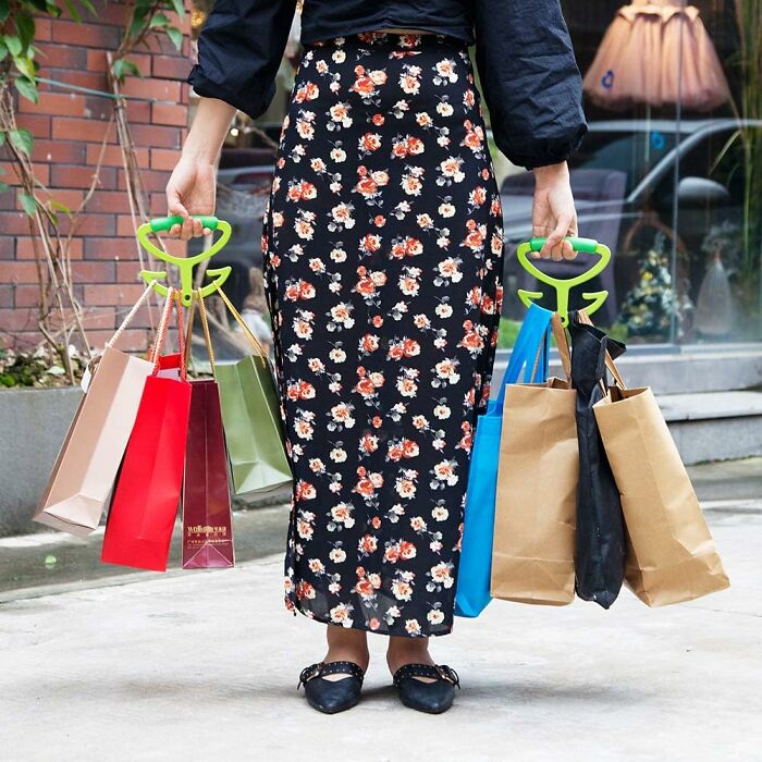 Person holding multiple shopping bags with green handles, wearing a floral skirt, embodying solo life essentials.