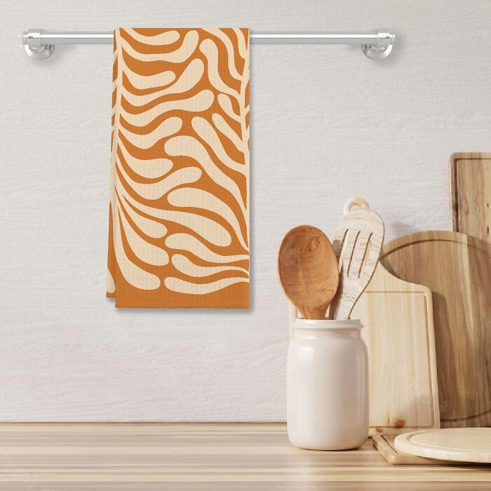 Orange and beige patterned towel hanging, with wooden utensils and cutting boards on the countertop.