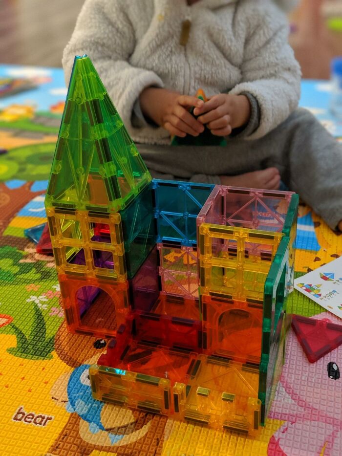 Colorful magnetic building tiles assembled into a structure, a child playing with popular toys kids genuinely can't get enough of.