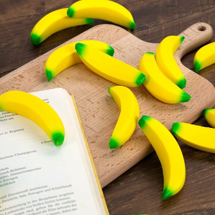 Bright yellow food-shaped objects resembling bananas scattered on a wooden cutting board and beside an open book