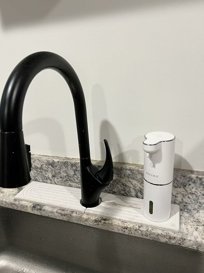 Automatic soap dispenser next to a modern black faucet on a granite countertop.