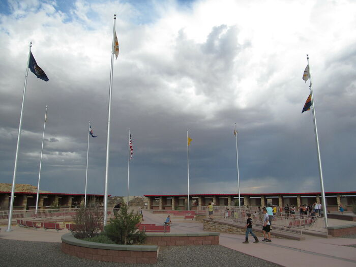 Tourists at Four Corners Monument under cloudy sky, flags flying high, showcasing a FOMO-induced travel experience.