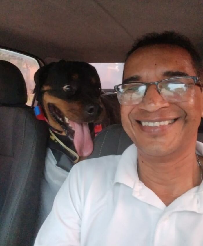 Man in glasses smiling with a Rottweiler in a pet taxi selfie.